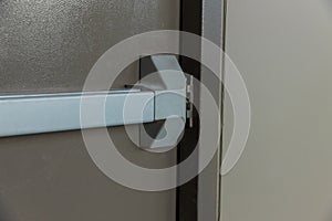 Emergency fire exit door. Closed up latch and rusty door handle of emergency exit. Push bar and rail for panic exit. Open one way