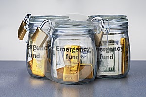 Emergency fund in three glass jars with cash and gold bars.