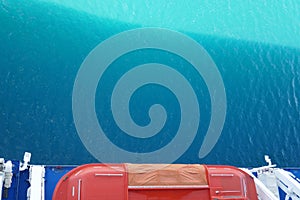 Emergency life boat hanging over side of cruise ship with tropical blue ocean water