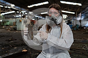 emergency pollution factory concept. Female chemist wearing PPE and gas mask inspecting oil on factory floor