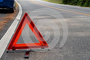 Emergency red warning triangle on the road sign with the white road line and broken car