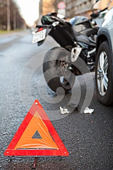 Emergency road triangle sign is on asphalt, road accident with car and motorcycle