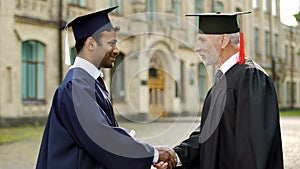 Eminent professor giving diploma to male student shaking hand, successful future photo
