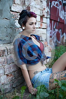 Emo girl in pin-up sits near a brick wall