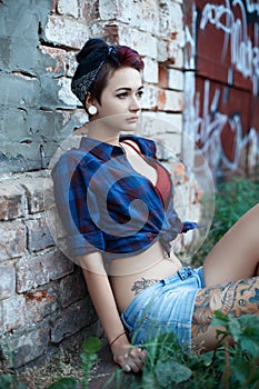 Emo girl in pin-up sits near a brick wall