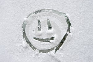 The emoticon is drawn on the glass covered with snow.