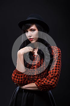 Emotion brunette female model posing in black hat with red bright lipstick on black background. Art fashion portrait.