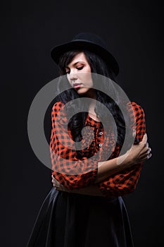 Emotion brunette female model posing in black hat with red bright lipstick on black background. Art fashion portrait.