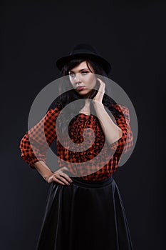 Emotion brunette female model posing in black hat with red bright lipstick on black background. Art fashion portrait.