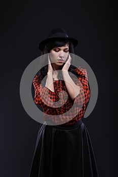 Emotion brunette female model posing in black hat with red bright lipstick on black background. Art fashion portrait.