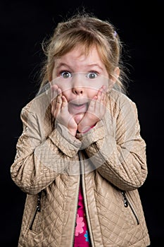 Emotion concept: astonished little girl. Black background, studio photo.