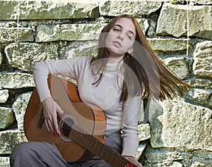 Emotion concept. Portrait of a young girl playing the guitar in front of stone wall