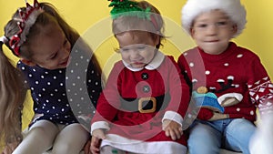 Emotion Cute Happy 3 Siblings Friend Baby Girl And Boy Wave Feet In Santa Suit Looking On Camera At Yellow Background