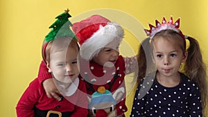 Emotion Cute Happy 3 Siblings Friends Baby Girl Boy Kissing Hug In Santa Suit Looking On Camera At Yellow Background