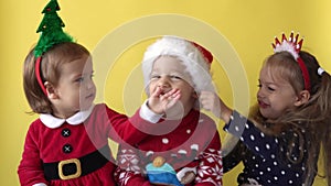 Emotion Cute Happy 3 Siblings Friends Baby Girl Boy Kissing Hug In Santa Suit Looking On Camera At Yellow Background
