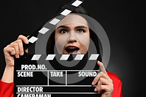 Emotional actress with clapperboard on black background. Film industry