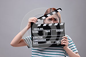 Emotional actress with clapperboard on grey background. Film industry