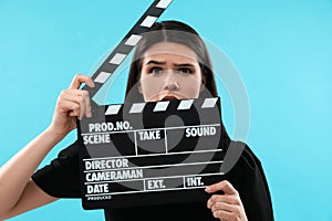 Emotional actress with clapperboard on light blue background. Film industry