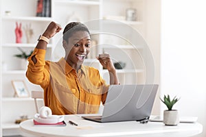 Emotional african american businesswoman celebrating success, working on laptop