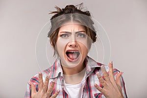 Emotional angry young woman screaming on gray background. Hate and rage emotions, facial expression concept.