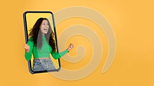 Emotional Arabic Woma In Smartphone Screen Shaking Fists, Yellow Background