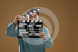 Emotional asian actor with clapperboard on brown background, space for text. Film industry