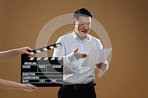 Emotional asian actor performing role while second assistant camera holding clapperboard on brown background. Film industry