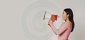 Emotional asian woman shouting in megaphone over grey background