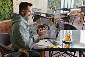 Emotional bearded man in casual clothes in cafe using his laptop. Work from anywhere concept