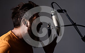 Emotional bearded man singing to condenser microphone in studio. Professional male vocalist. Music.