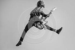 emotional bearded rock musician playing electric guitar in leather jacket and jumping, guitar player