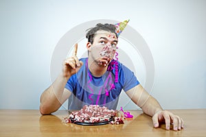 Emotional beautiful caucasian man with birthday party cone hat on head and crumple cake raises your index finger up. People and li