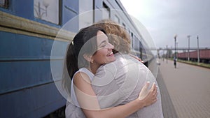 Emotional beautiful girl embrace guy and laughs near railway carriage on Train Station after separation