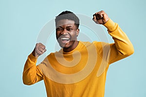 Emotional black guy raising fists up on blue
