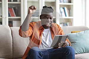 Emotional black man holding digital tablet and gesturing, home interior