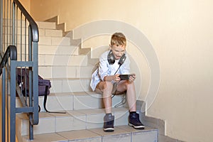 An emotional boy in a shirt is sitting on the stairs , looking at the phone, shouting