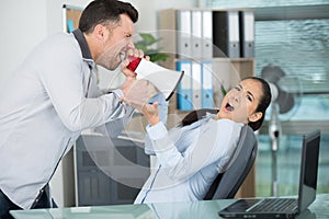 emotional businessman shouting with megaphone at frightened female colleague