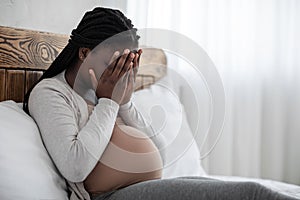Emotional changes during pregnancy. Upset black pregnant woman covering face with hands