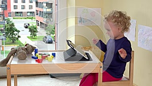 Emotional child using tablet computer. Poor teddy bear laying on table