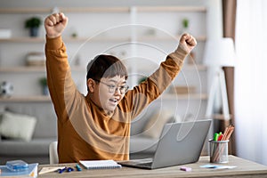 Emotional chubby asian schooler celebrating success, using notebook