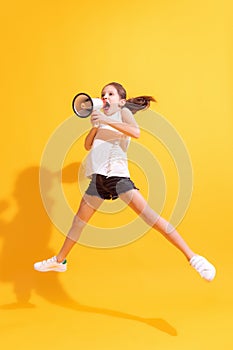 Emotional cute girl, kid shouting at megaphone isolated on bright yellow background. Concept of news, holidays, vacation