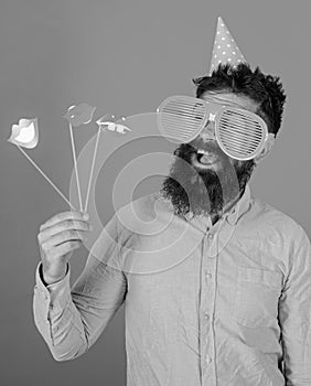 Emotional diversity concept. Man with beard on cheerful face holds smiling lips on sticks, red background. Guy in party