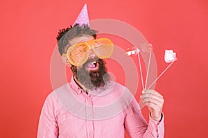 Emotional diversity concept. Man with beard on cheerful face holds smiling lips on sticks, red background. Hipster in