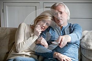 Emotional elderly couple watching drama on TV at home