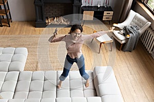 Emotional energetic young hispanic woman dancing on sofa.