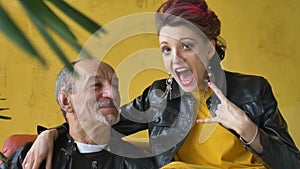 Emotional family portrait of adult daughter and senior father in loft room wearing black leather jackets in punk style