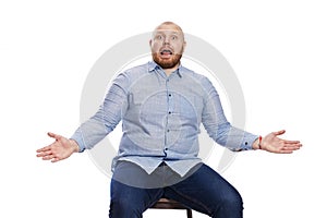 Emotional fat red man with a beard in a blue shirt and jeans. Opening his mouth shrugs and looks at the camera.  over