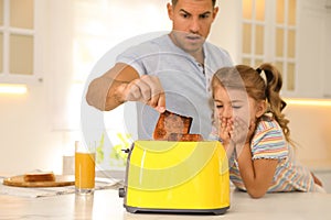 Emotional father and daughter near toaster with slices of burnt bread in kitchen