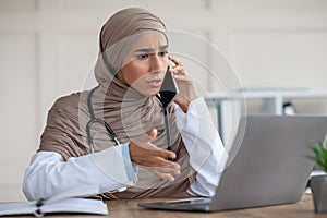 Emotional female doctor looking at laptop screen, talking on phone