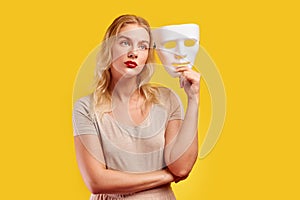 Emotional female person with white mask on yellow background. Internet fraud concept, anonymous, incognito, bipolar personality di